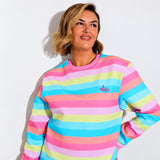 A woman wearing a pastel striped crewneck sweatshirt with horizontal bands of pink, light blue, yellow, and lavender, featuring a small pink embroidered logo on the left chest, set against a plain white background.