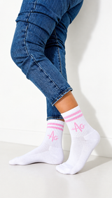 White ankle socks with pink stripes and pink monogram lettering, worn with blue jeans against a clean white wall.