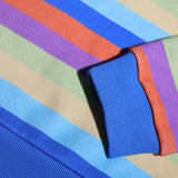 Close-up of a striped fabric garment, showing diagonal bands of blue, purple, orange, beige, and light blue, with a ribbed blue cuff.